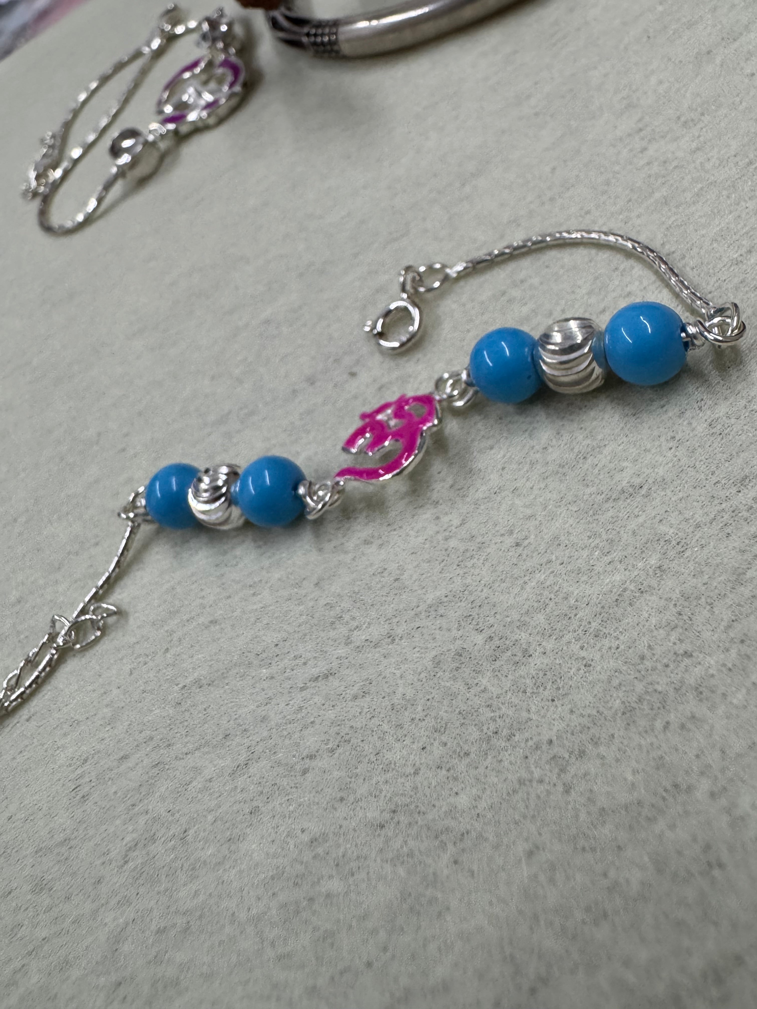 The full sterling silver beaded bracelet curved on grey felt, showing four blue beads, two fluted rondelles and the enamel Om at the centre.