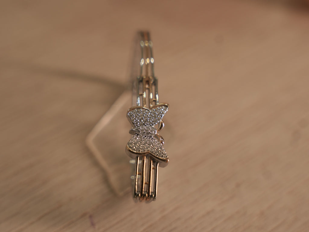 Sterling silver bracelet with a pave set American Diamonds butterfly on a three rail band with rose-tone bars.