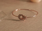 Slim rose-tone wire bracelet with a pave set American Diamonds crescent moon curled around a star.