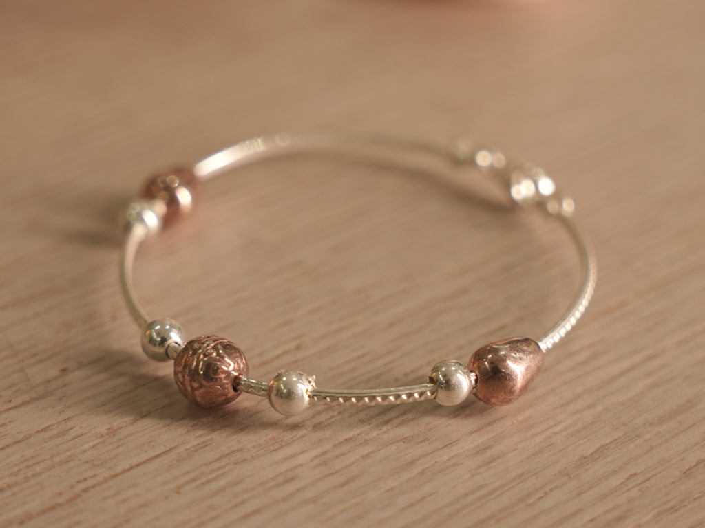 Flexible silver snake chain bracelet with polished silver beads, rose-tone beads and a small heart.