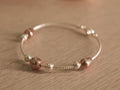 Flexible silver snake chain bracelet with polished silver beads, rose-tone beads and a small heart.