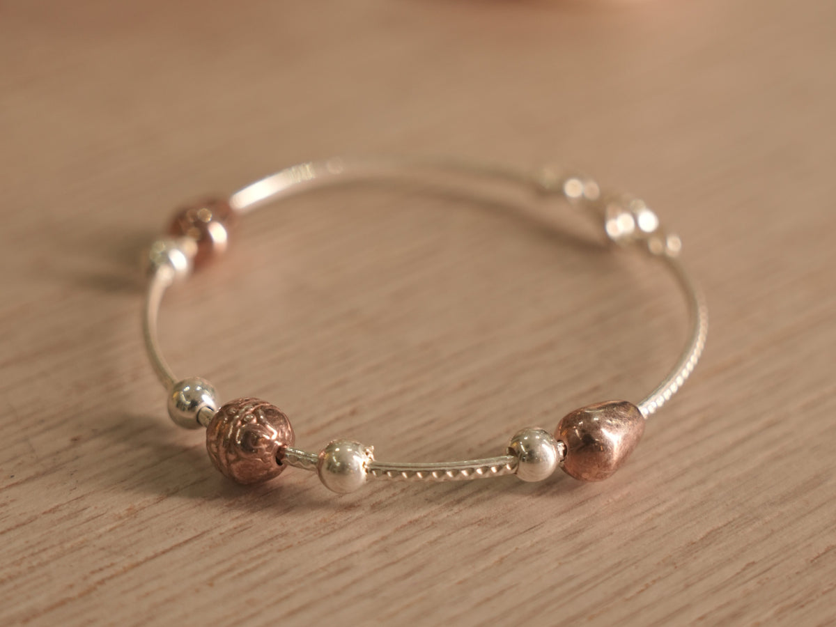 Flexible silver snake chain bracelet with polished silver beads, rose-tone beads and a small heart.