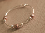 Close view of the textured rose-tone beads and heart along the snake chain bracelet.