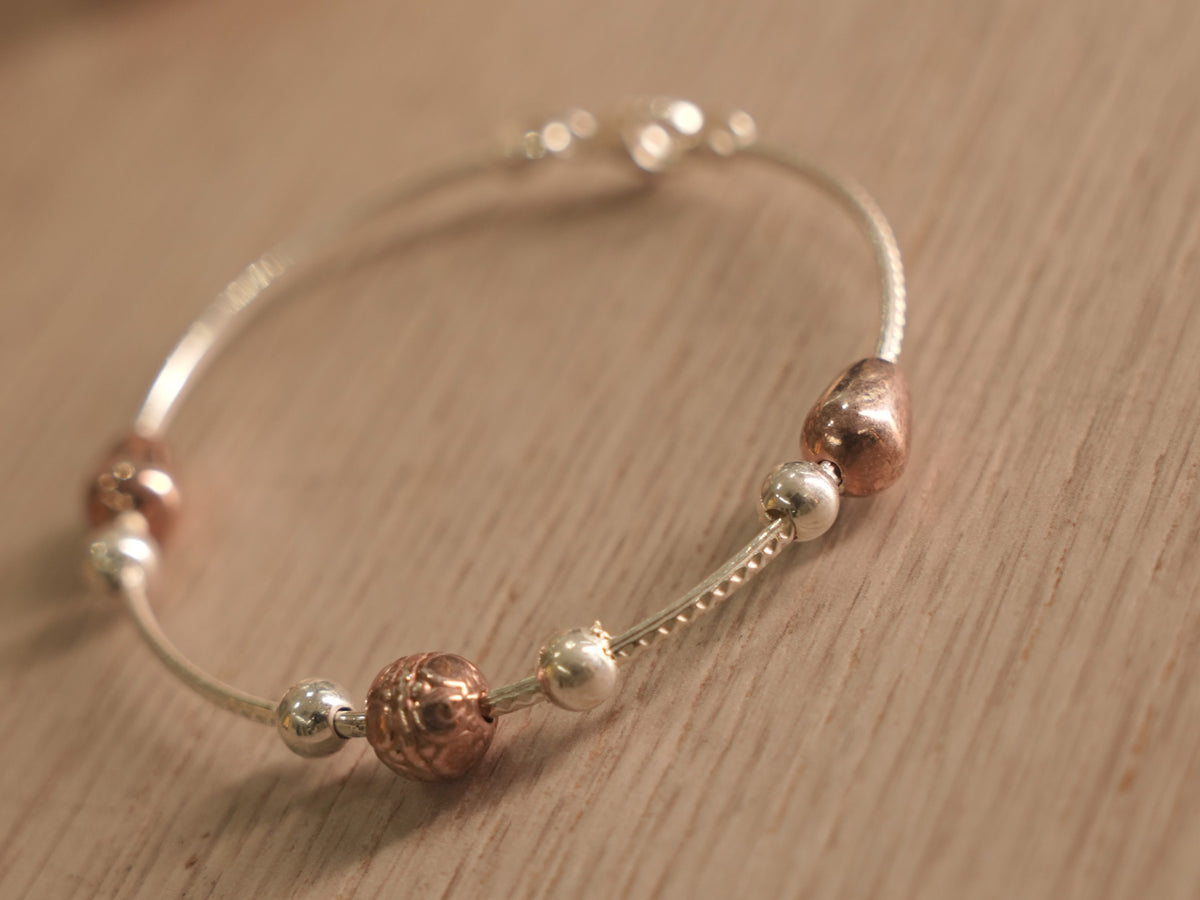 Close view of the textured rose-tone beads and heart along the snake chain bracelet.