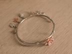 Close view of a rose-tone lily with pave set petals on the silver bracelet.