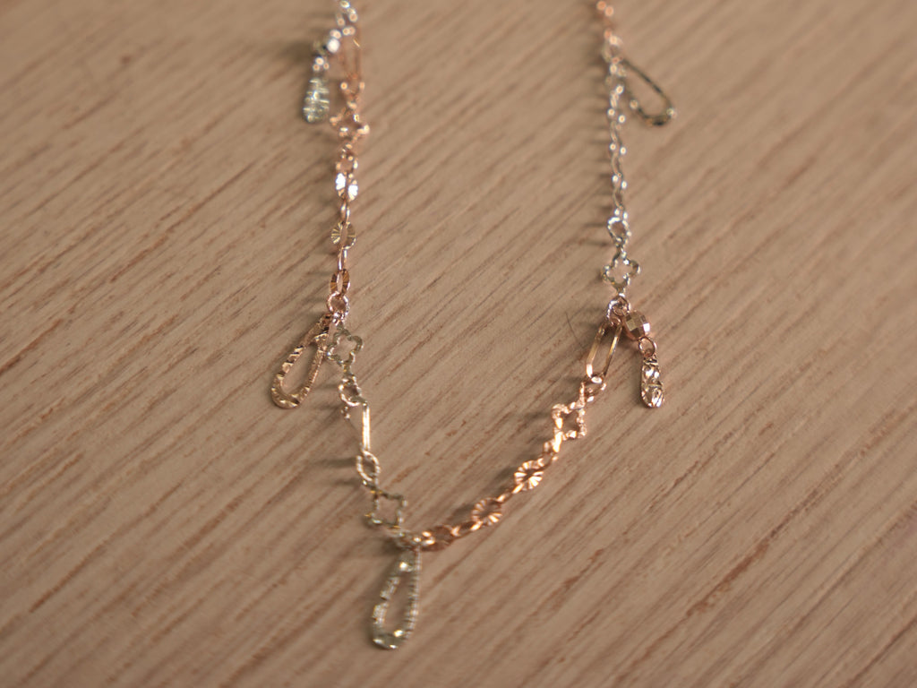 Delicate two-tone chain bracelet with starburst discs, clover links and safety pin shaped connectors.