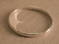 Plain polished sterling silver kids kada standing on a pale wooden surface.