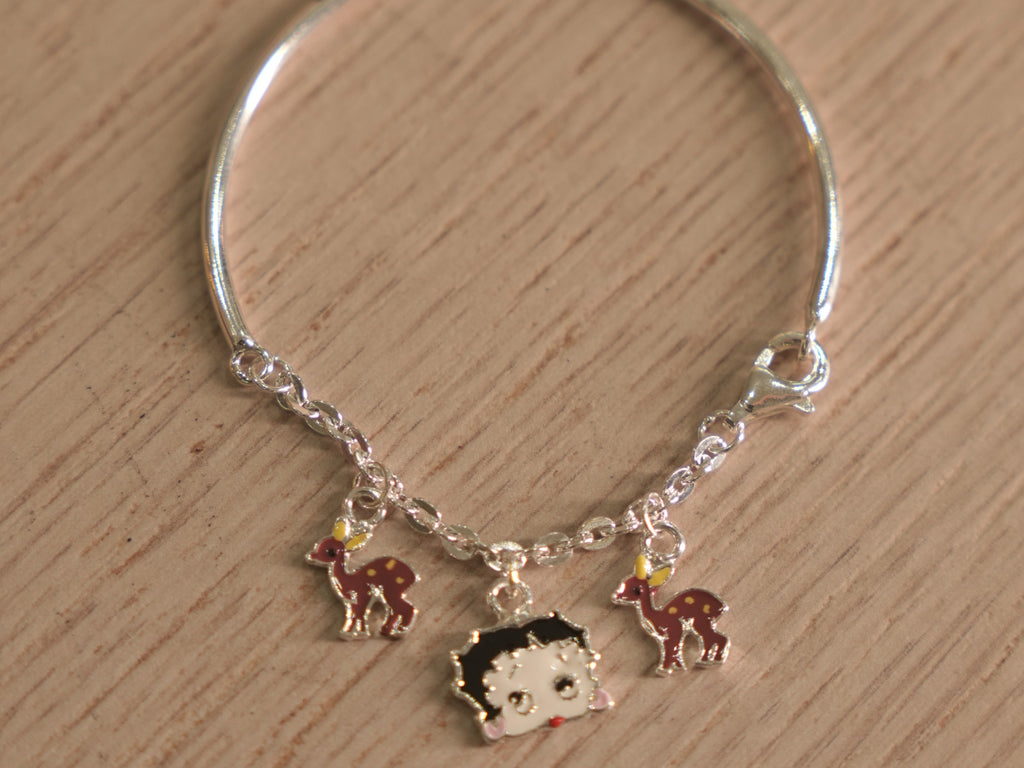 Kids silver bracelet with a chain section carrying enamelled deer charms and a cartoon doll face.