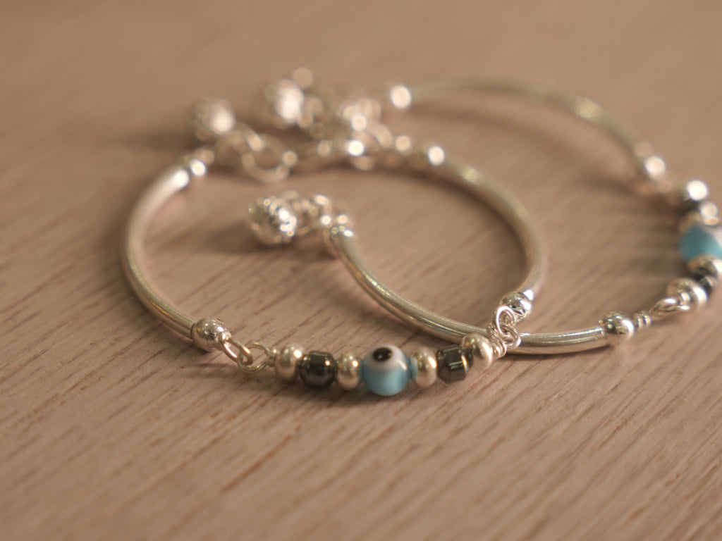 Close view of the evil eye glass bead between dark beads on the baby bangle.