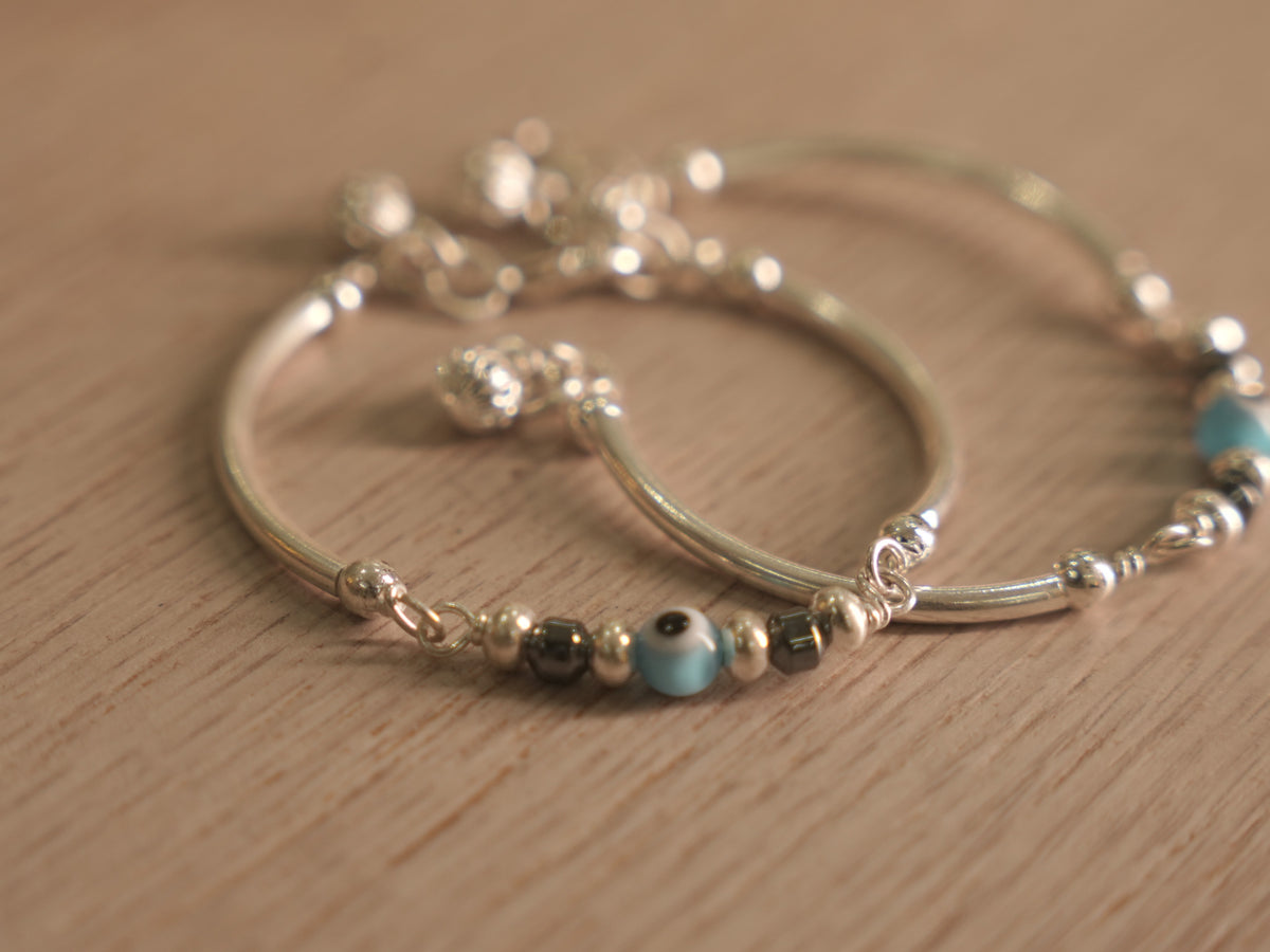 Close view of the evil eye glass bead between dark beads on the baby bangle.