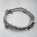 Sterling silver twin-tube kada with diamond-cut sections and small leaf and bead charms, seen at an angle.