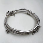 Sterling silver twin-tube kada with diamond-cut sections and small leaf and bead charms, seen at an angle.