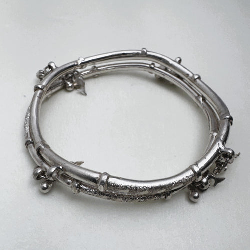 Sterling silver twin-tube kada with diamond-cut sections and small leaf and bead charms, seen at an angle.