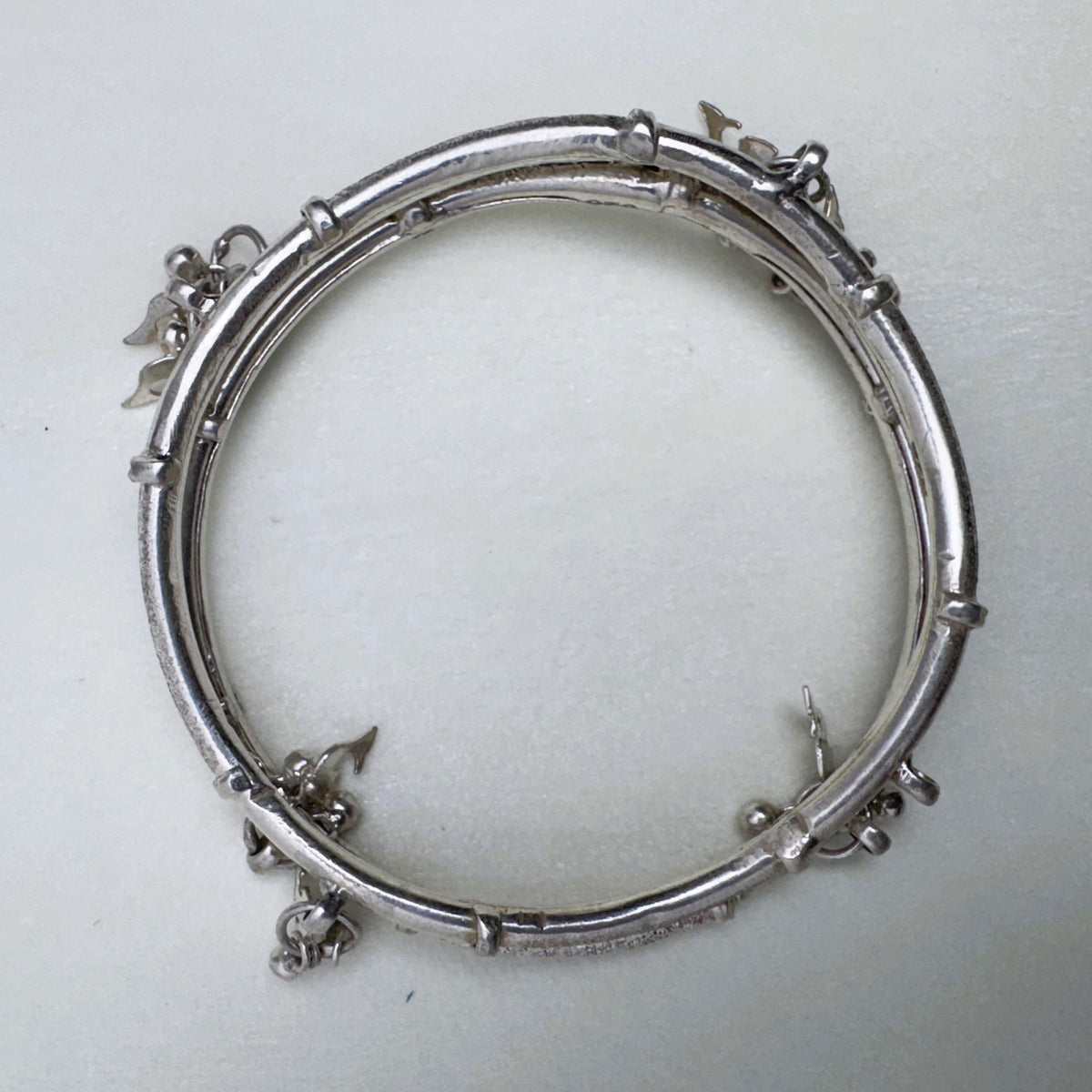 The twin-tube silver kada seen from above, showing the charms at the joints.