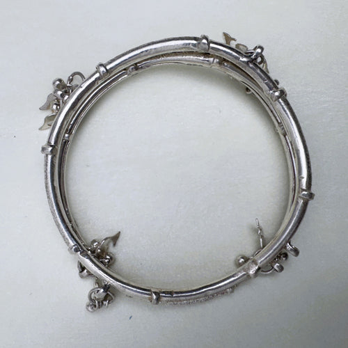 The twin-tube silver kada seen from above, showing the charms at the joints.