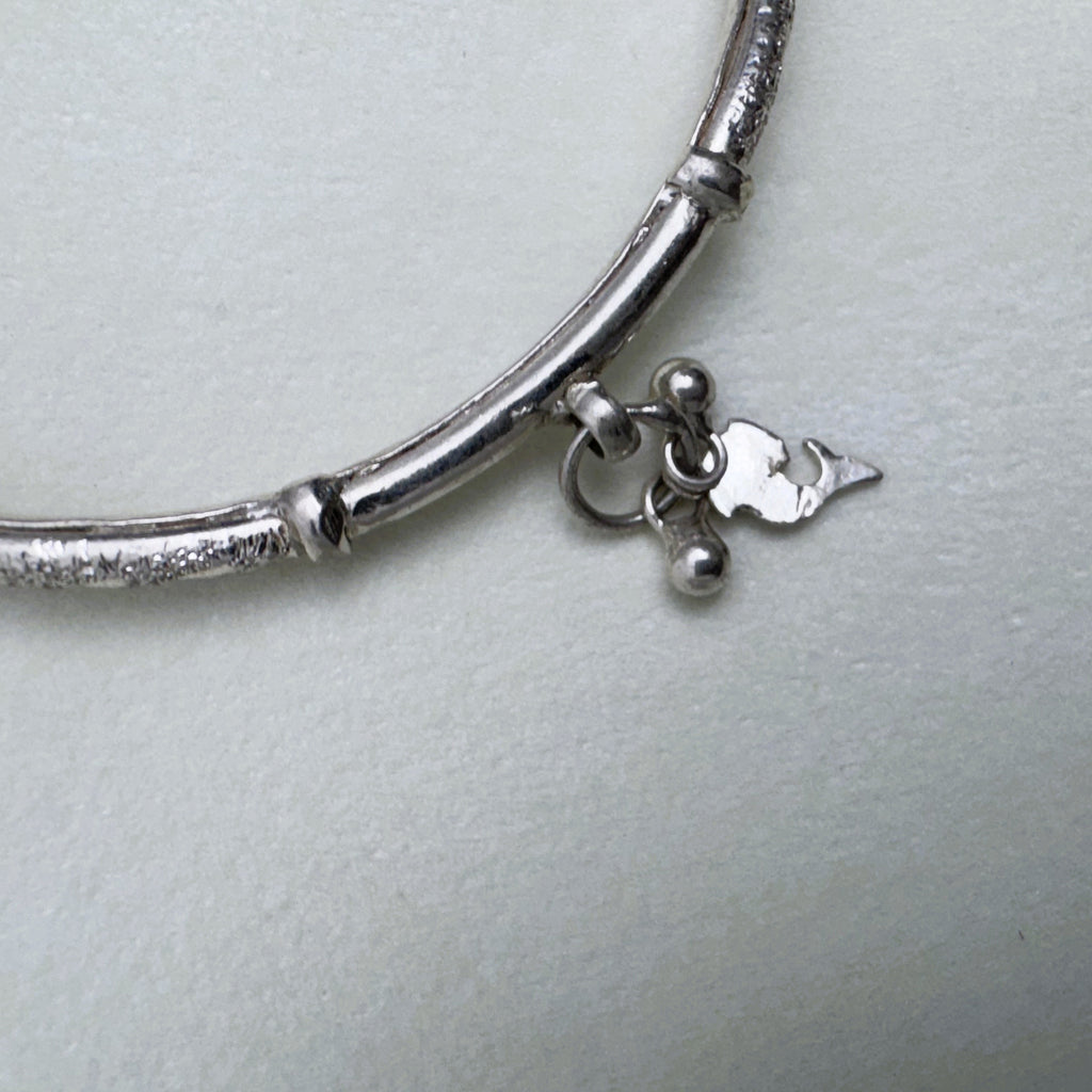 Close view of a leaf and bead charm hanging from a joint on the silver kada.