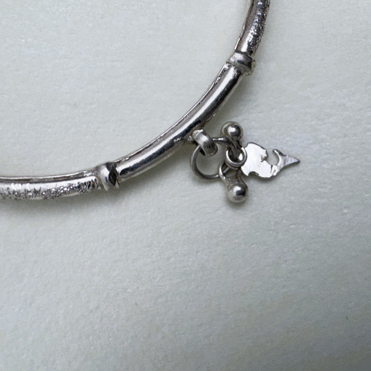 Close view of a leaf and bead charm hanging from a joint on the silver kada.