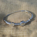 Sterling silver hinged bangle bracelet with three crown medallions and American Diamond pave links, on cream fabric.