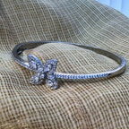 Sterling silver hinged bangle bracelet with a four-petal American Diamond flower and a pave set half, on cream fabric.