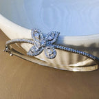 The flower bangle resting against a white bowl, showing the marquise petals and the pave set band.