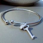 Sterling silver open cuff bracelet with ball ends, a pave key charm and a cartoon character charm, on a grey surface.