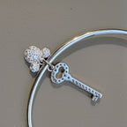 The key and cartoon charms hanging from the slim silver cuff, seen from the back.