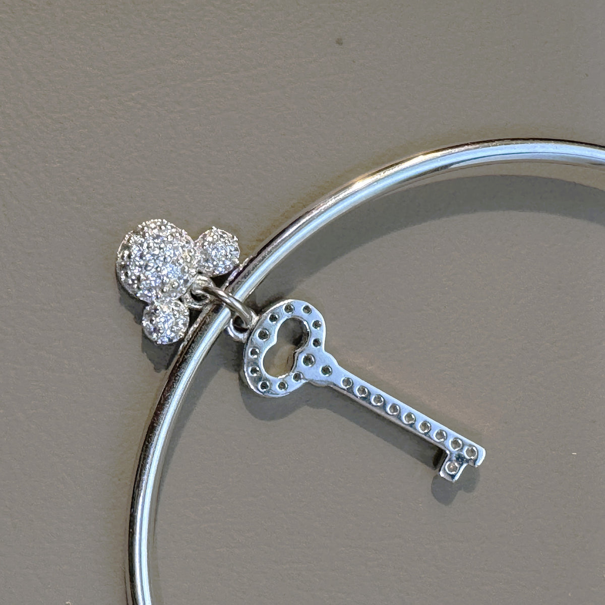 The key and cartoon charms hanging from the slim silver cuff, seen from the back.