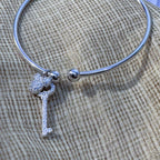 The silver open cuff with its two charms resting on cream fabric.