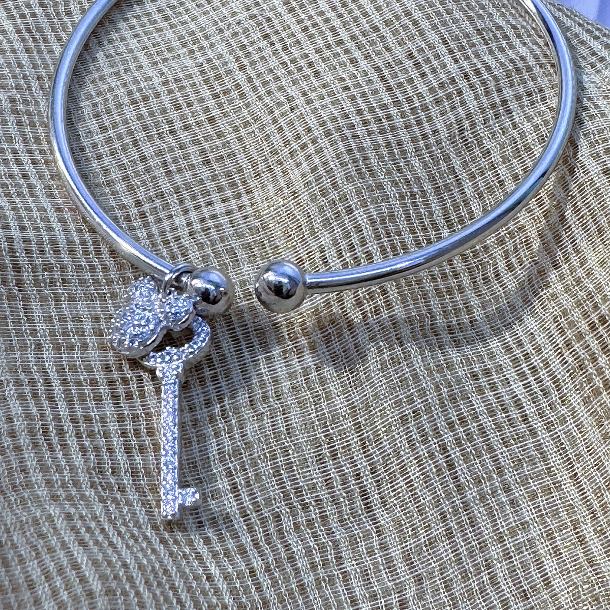 The silver open cuff with its two charms resting on cream fabric.