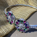 Sterling silver open cuff bracelet with two meenakari-style flowers of multicolour stones, on cream fabric.
