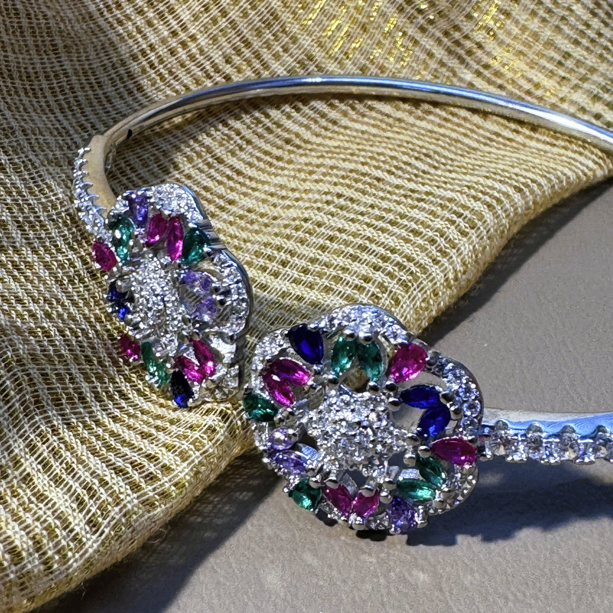 Sterling silver open cuff bracelet with two meenakari-style flowers of multicolour stones, on cream fabric.