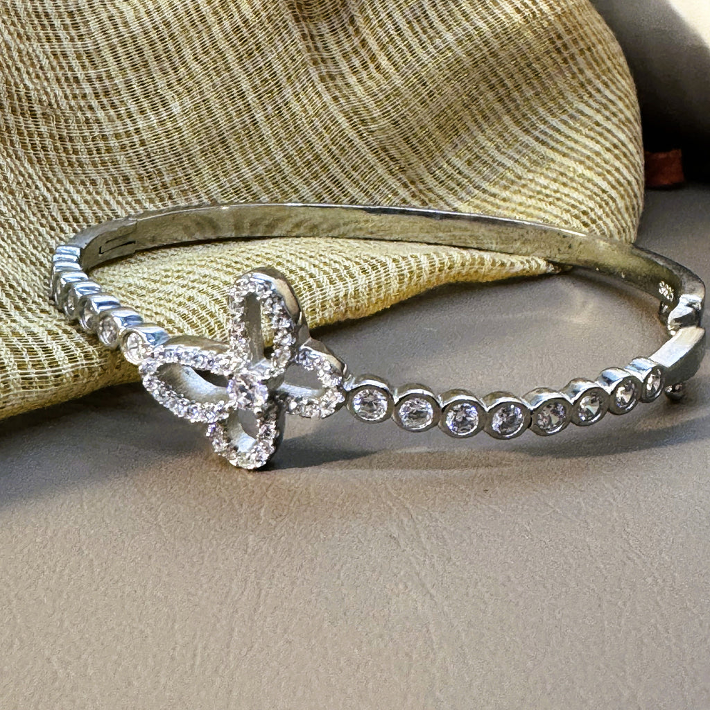 Sterling silver hinged bangle bracelet with an open pave set clover and bezel set stones, on cream fabric.