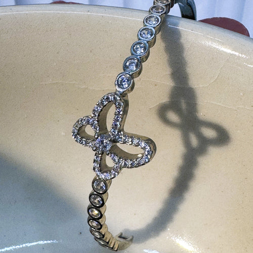 The clover bangle resting in a white bowl, showing the bezel set stones along the band.