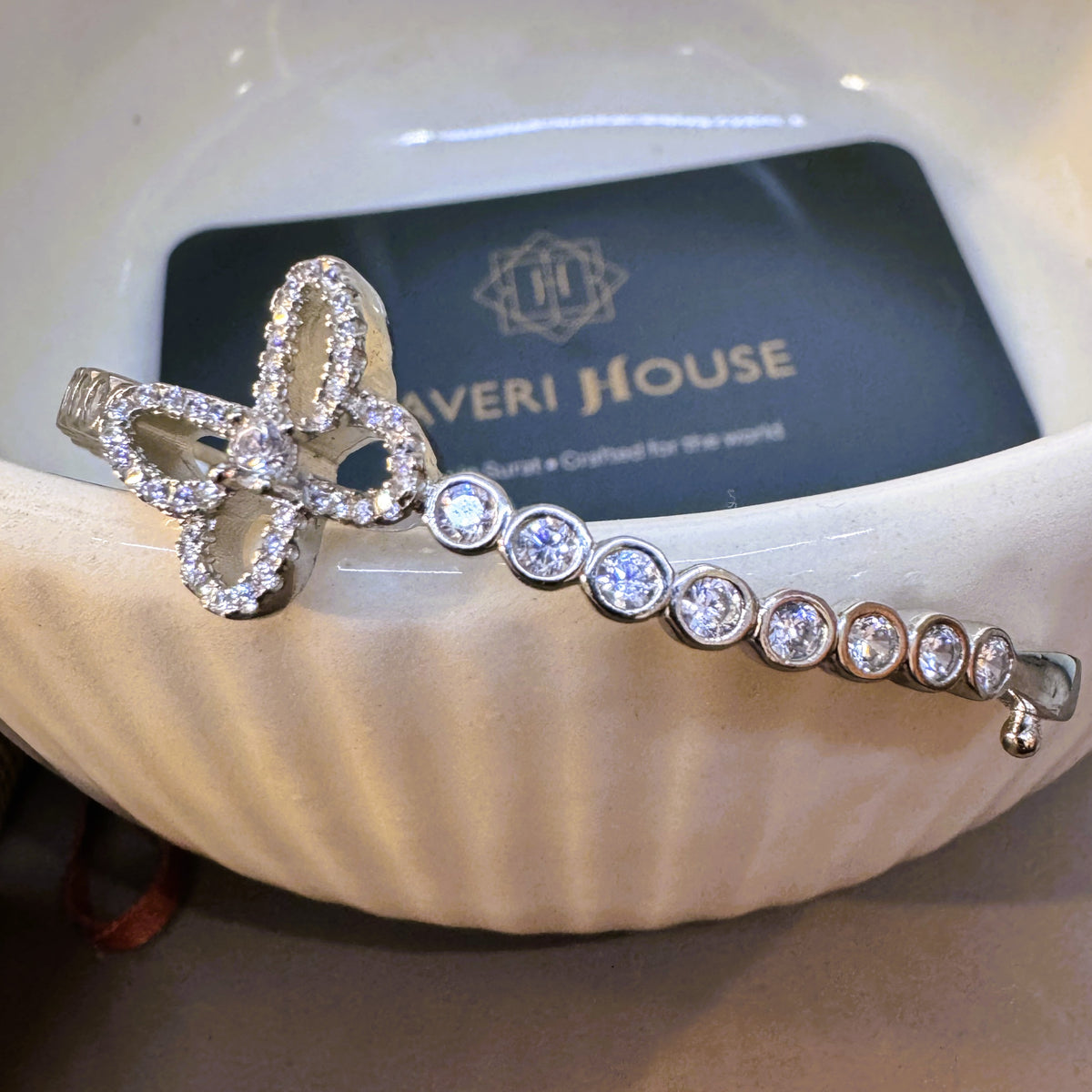 The silver clover bangle on a white dish with the Javeri House card behind it.