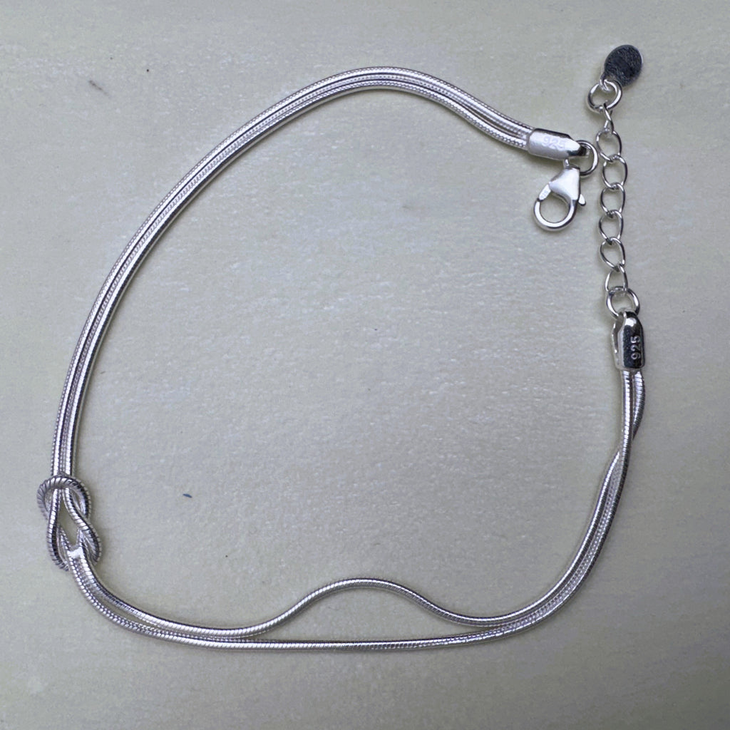 Sterling silver double snake chain bracelet with a love knot, laid open with the lobster clasp and extender.