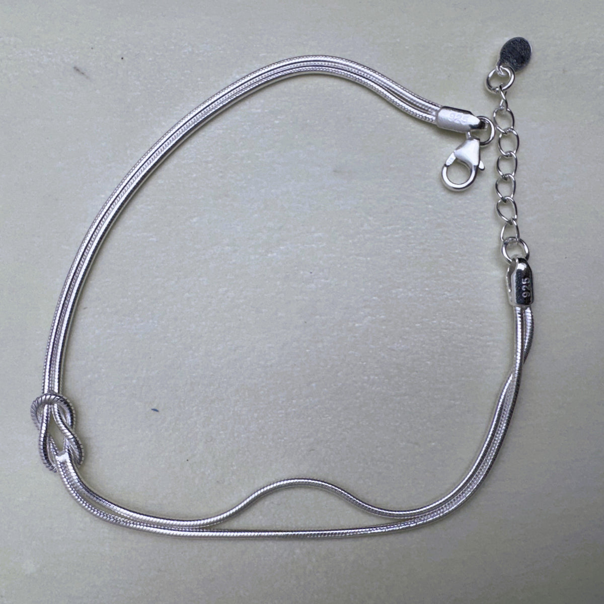 Sterling silver double snake chain bracelet with a love knot, laid open with the lobster clasp and extender.