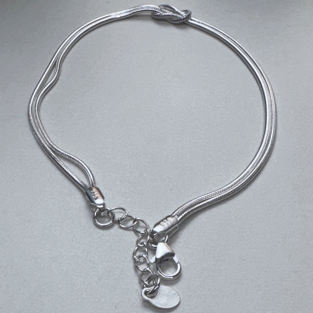 The love knot bracelet laid in a loop with the clasp and extender chain at the bottom.