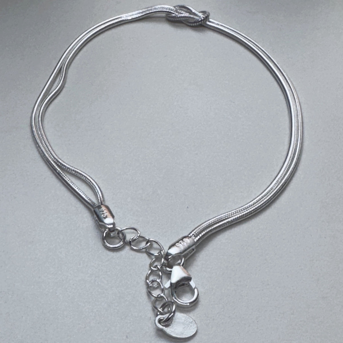 The love knot bracelet laid in a loop with the clasp and extender chain at the bottom.