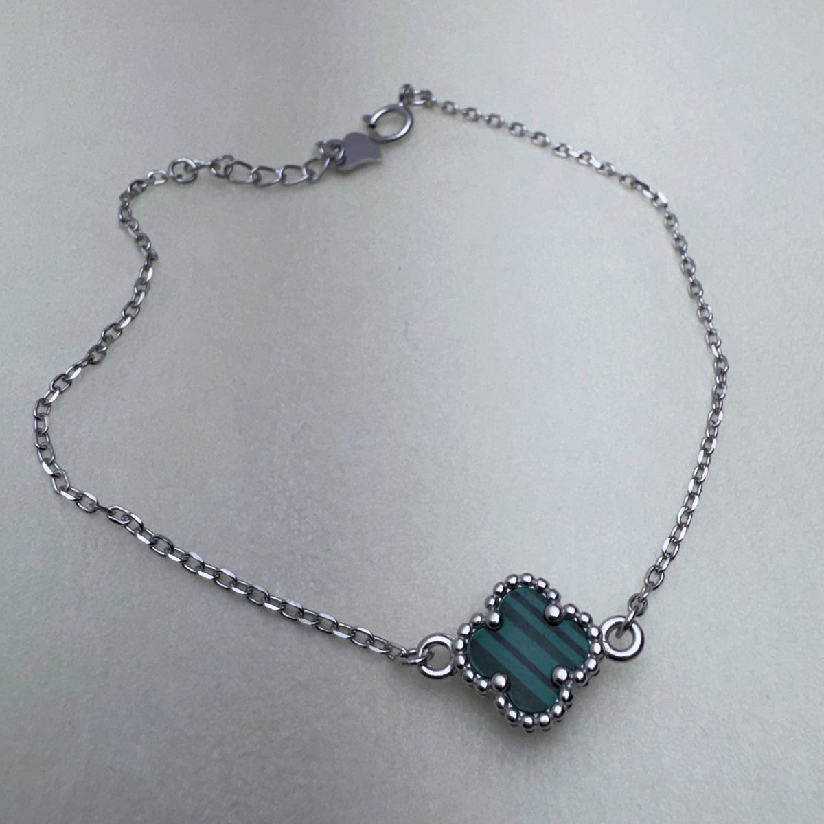 Sterling silver chain bracelet with a green glass clover in a beaded frame, laid in a loop with its clasp and extender.