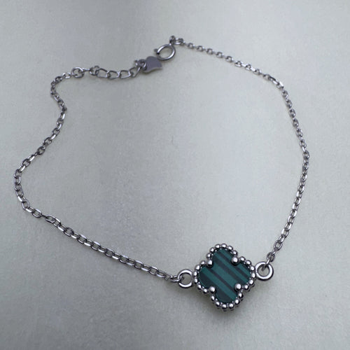 Sterling silver chain bracelet with a green glass clover in a beaded frame, laid in a loop with its clasp and extender.