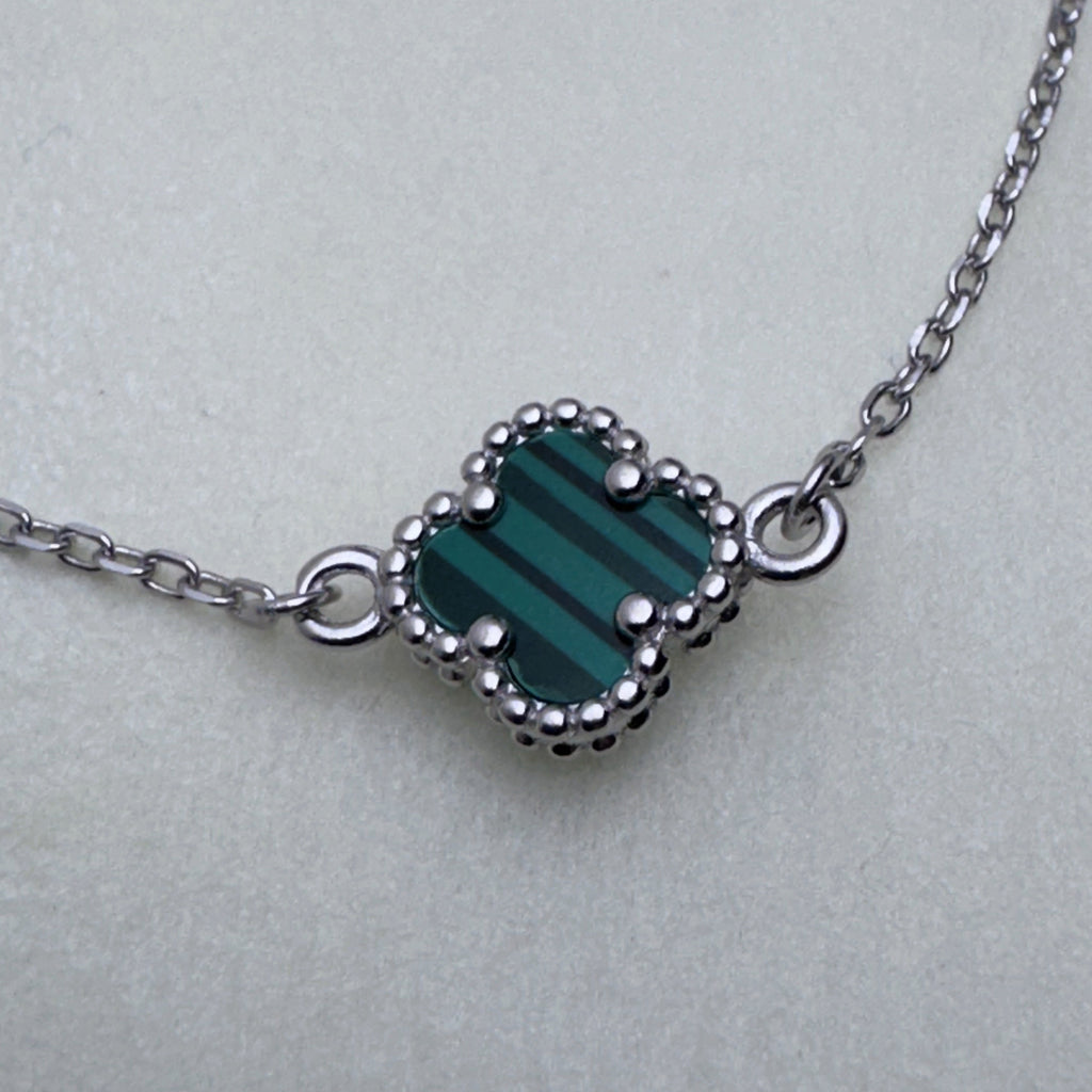 Close view of the green banded glass clover in its beaded silver frame on the cable chain.