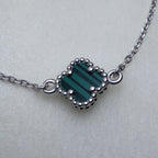 Close view of the green banded glass clover in its beaded silver frame on the cable chain.