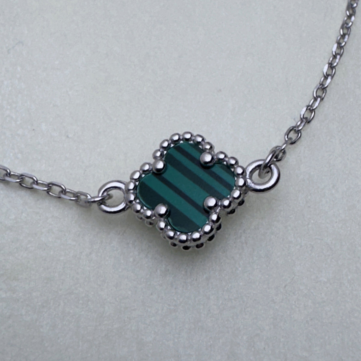 Close view of the green banded glass clover in its beaded silver frame on the cable chain.