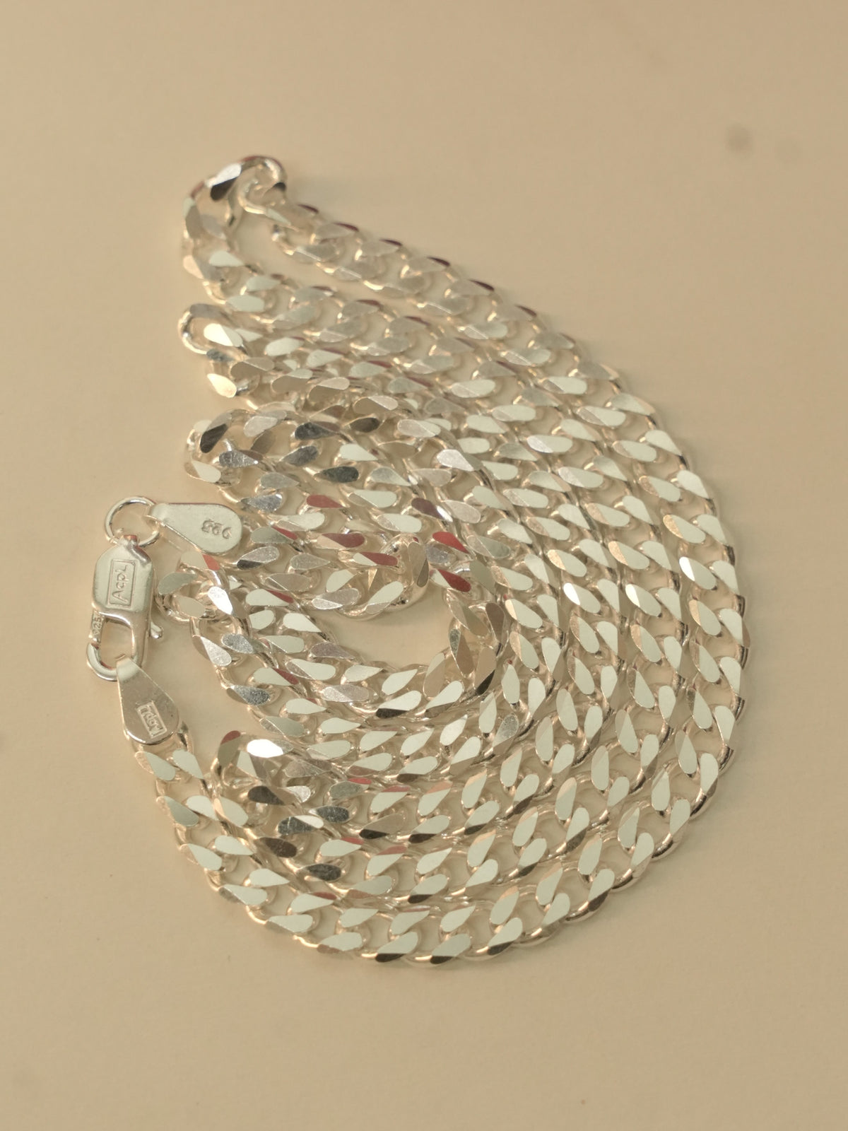 Sterling silver flat curb chain coiled on a pale surface, with the lobster clasp at the edge.
