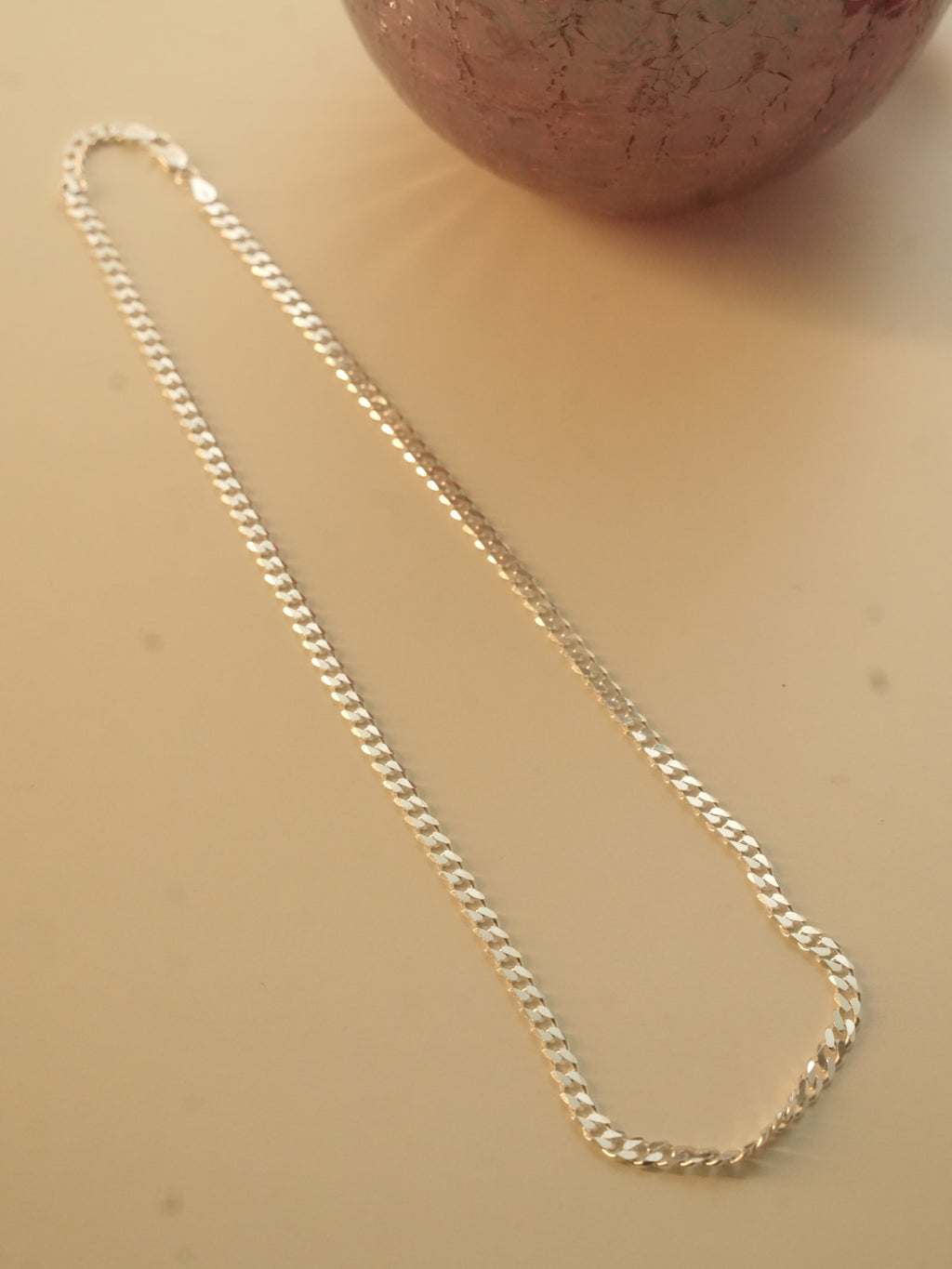 The silver curb chain laid out in a long loop beside a dark red glass vase.