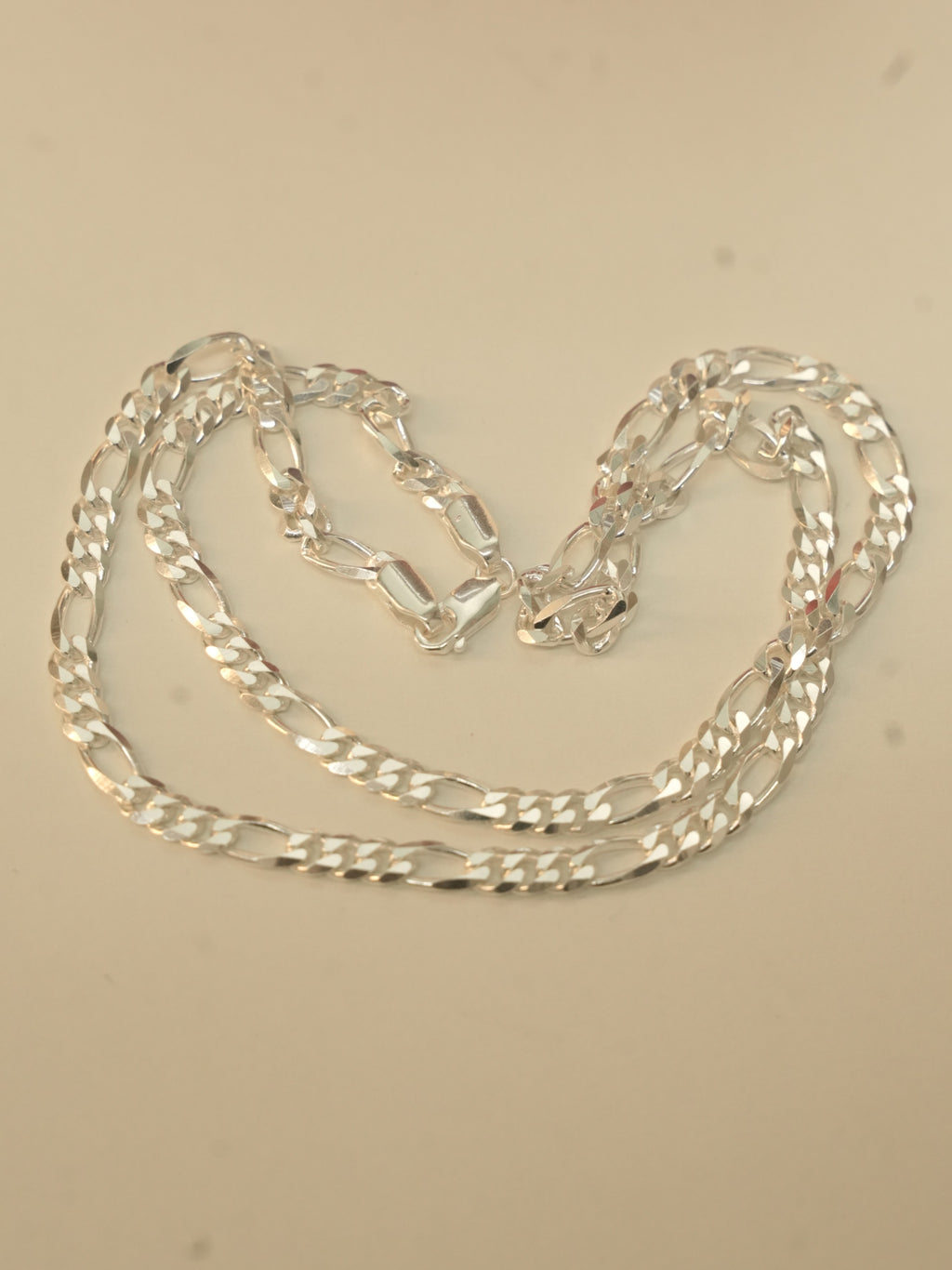 Sterling silver figaro chain laid in loose loops on a pale surface.