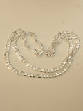 Sterling silver figaro chain laid in loose loops on a pale surface.