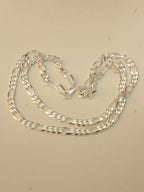 Sterling silver figaro chain laid in loose loops on a pale surface.