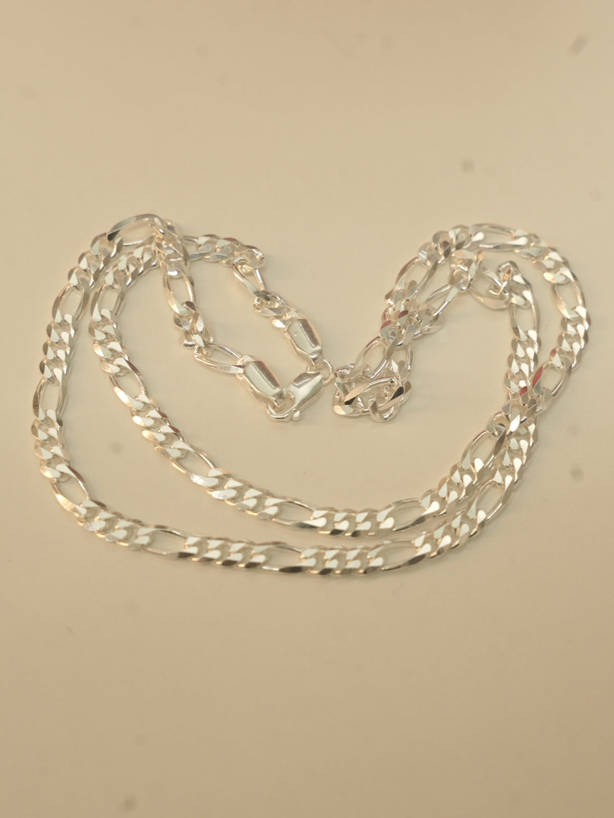 Sterling silver figaro chain laid in loose loops on a pale surface.
