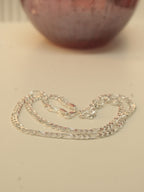 The silver figaro chain laid in loops beside a dark red glass vase.